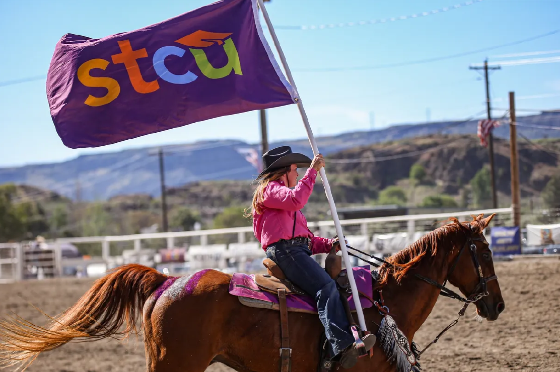 A woman riding a horse holding an STCU flag