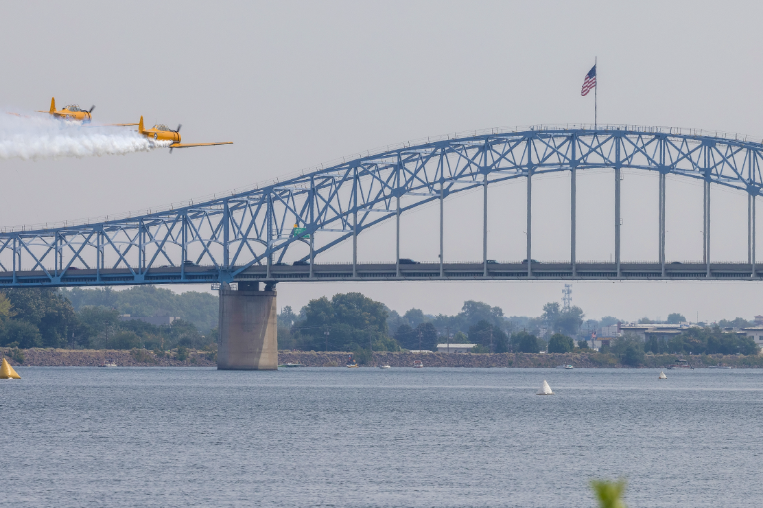 Photo of two yellow airplanes flying over a river near a bridge