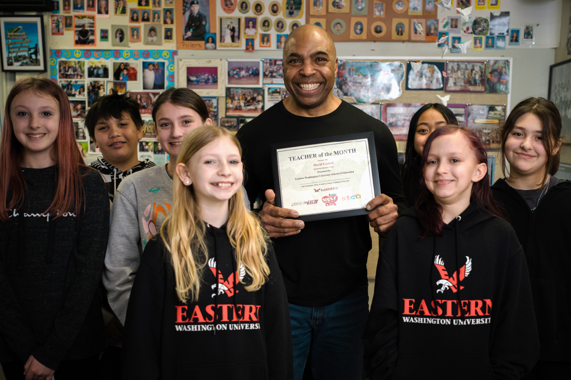 Photo of a teacher holding a plaque surrounded by his students