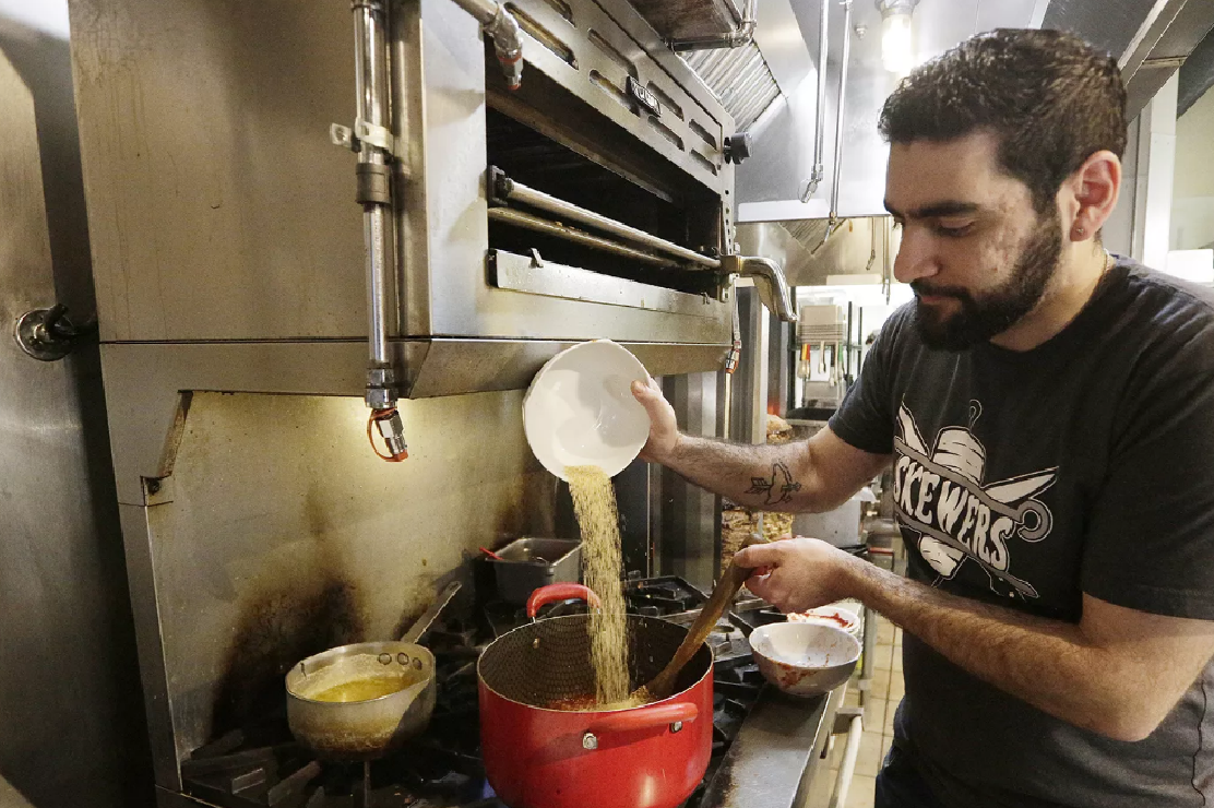 Photo of a cook pouring rice into a pot over a stove